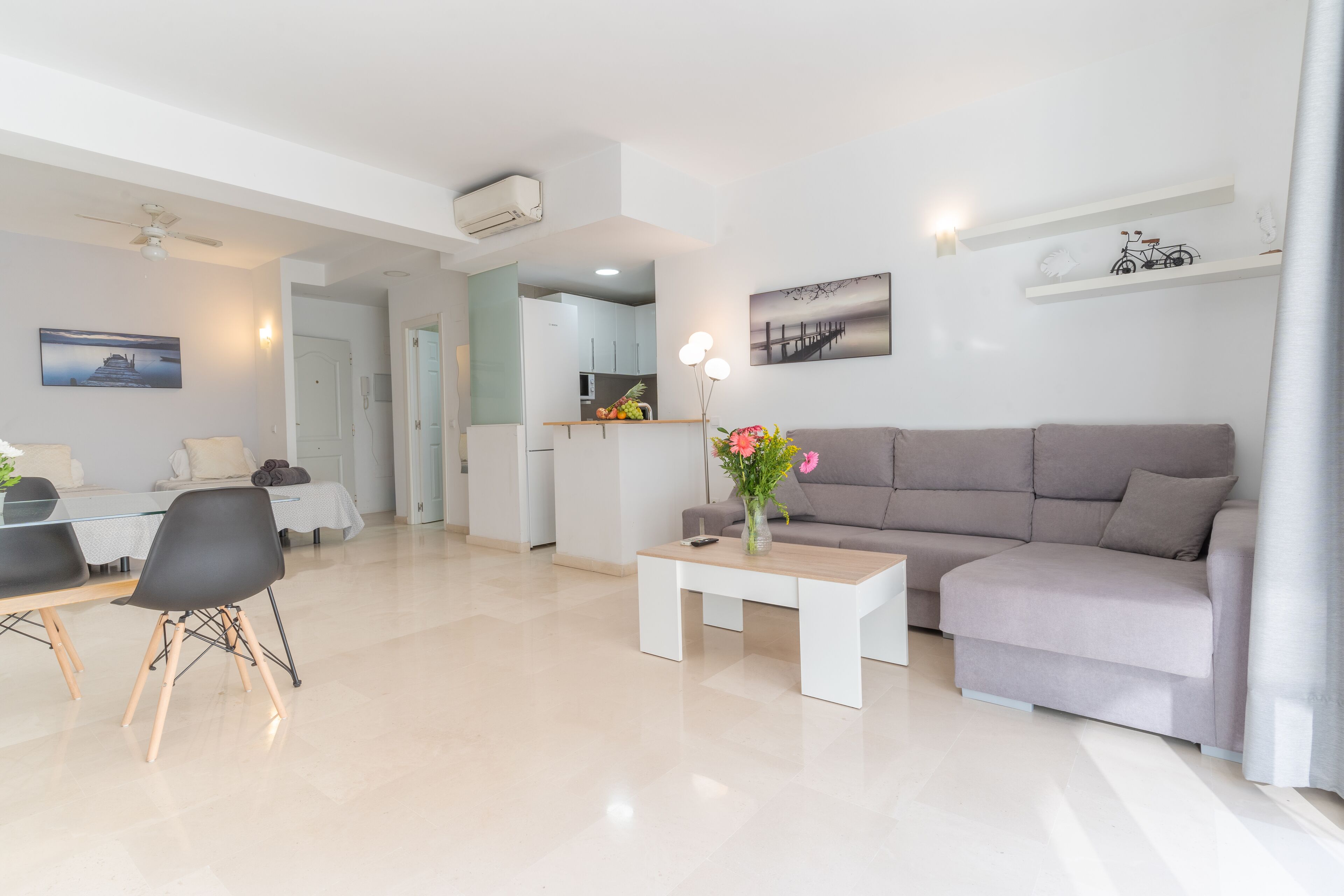 A modern living room with a grey sofa, a coffee table, and a dining area with a table and chairs.