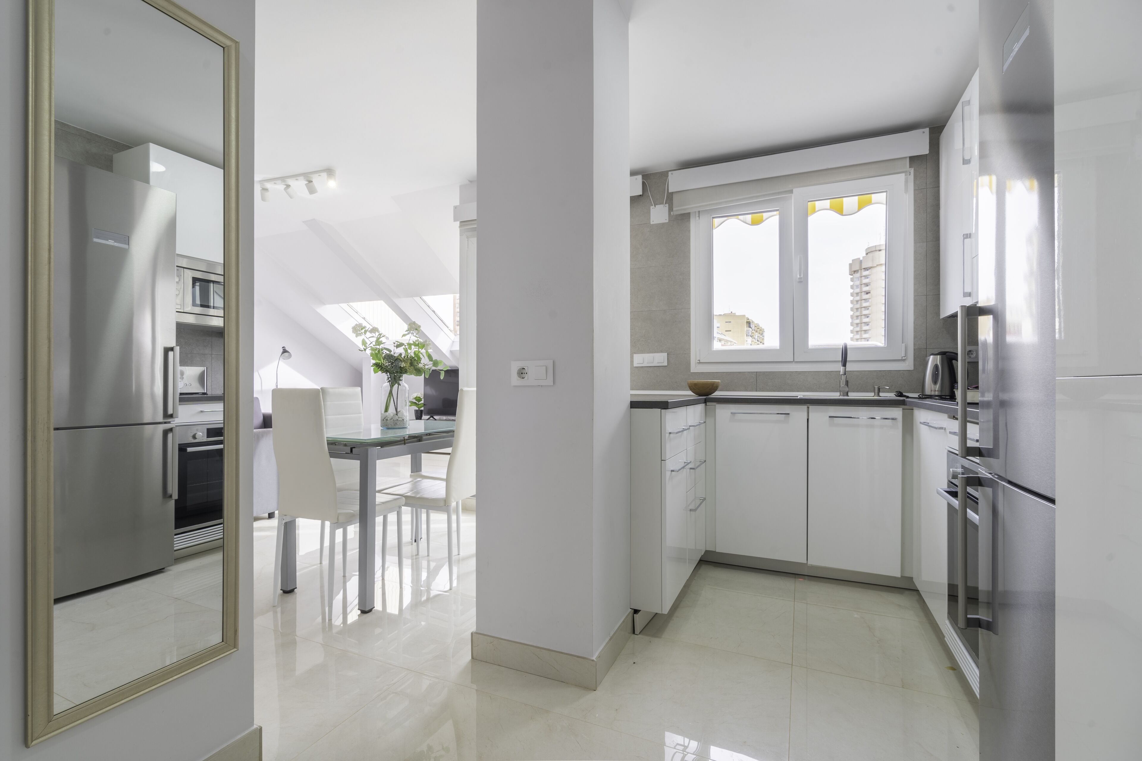 A modern kitchen with white cabinets, stainless steel appliances, and a large window providing natural light.