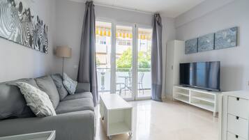 A modern living room with a grey sofa, a flat-screen TV, and a sliding glass door leading to an outdoor area.