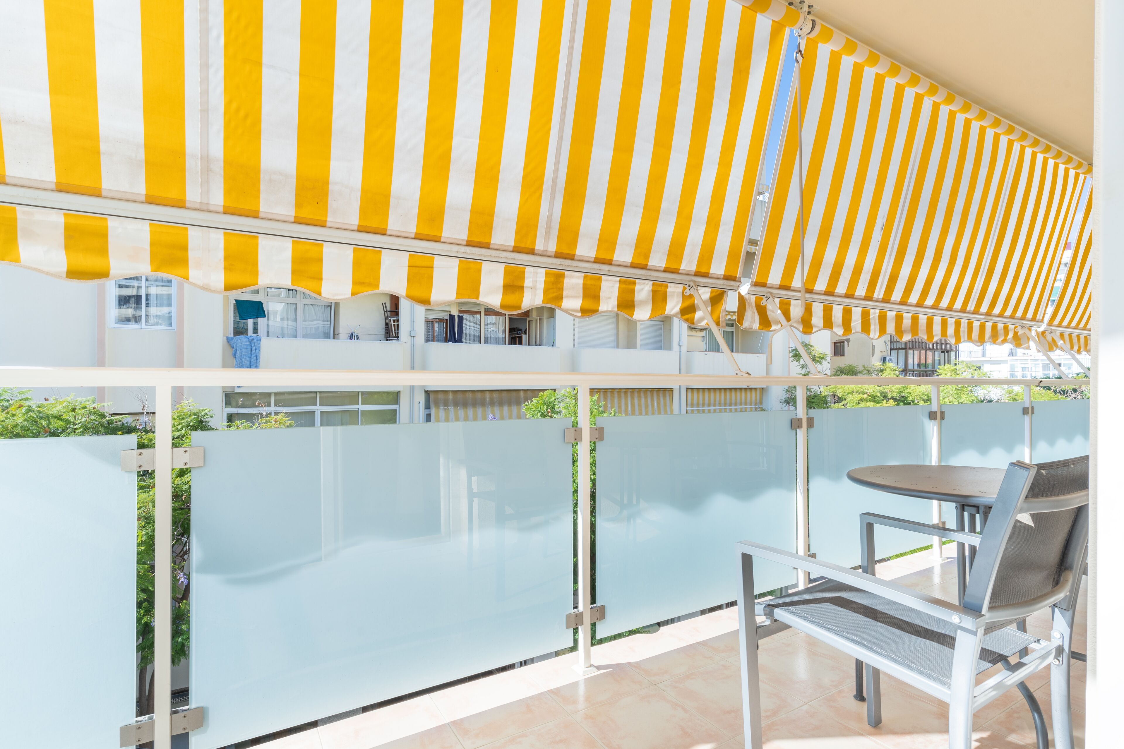 A balcony with a yellow-striped awning, a glass partition, and a metal chair.