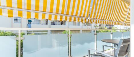A balcony with a yellow-striped awning, a glass partition, and a metal chair.