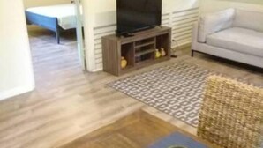 Un salon avec une table en bois, un canapé, un téléviseur posé sur un meuble et un lit à l’arrière-plan.