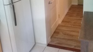 Un couloir avec un réfrigérateur blanc, un plancher en bois et une porte blanche.
