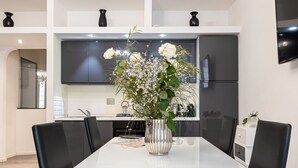 A modern dining area with a white table, black chairs, and a silver vase with white flowers.