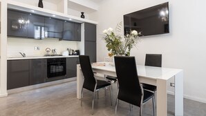 A modern kitchen with black cabinets, a white countertop, and a dining area with a white table and black chairs.