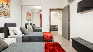 A modern hotel room with two beds, a flat-screen TV, a large mirror, and a view of the cityscape through the window.