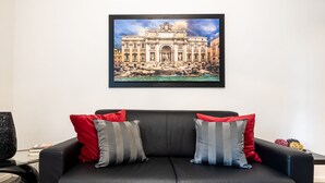 A black leather sofa with red and gray striped pillows, a framed picture of a historic building on the wall, and a round black table with a book and a decorative item.