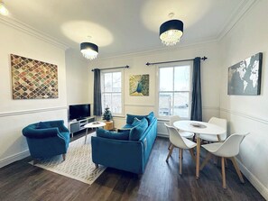 Een moderne woonkamer met een blauwe zithoek, een televisie en een kleine kerstboom.