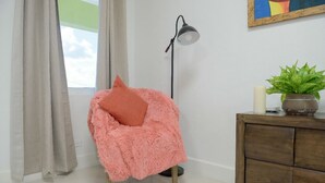 A cozy room with a fluffy pink chair, a floor lamp, a wooden cabinet, and a potted plant. - The Ideal Loft (Nassau)