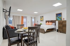 A modern hotel room with a dining area, a bed with orange pillows, and artwork on the walls. - The Ideal Loft (Nassau)