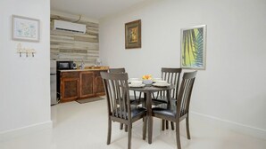 A dining area with a round table, four chairs, and a bowl of fruit. There is a kitchen in the background with a microwave and a wooden cabinet. - The Ideal Loft (Nassau)