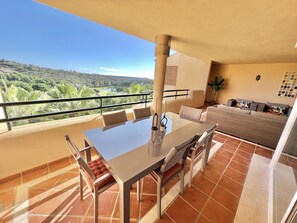 A balcony with a table and chairs, a sofa, and a view of a green landscape.