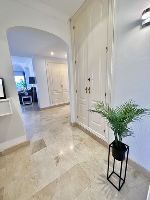 A hallway with a marble floor, white doors, and a potted plant.