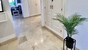 Un passadís amb sòl de marbre, portes blanques i una planta en test.