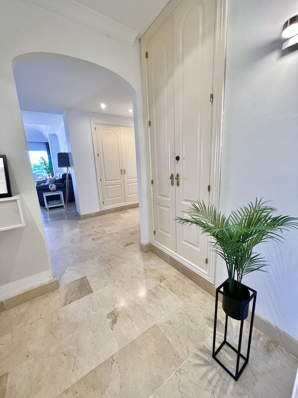 A hallway with a marble floor, white doors, and a potted plant.