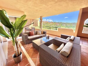 A spacious balcony with wicker furniture, a potted plant, and a clear view of a hillside.