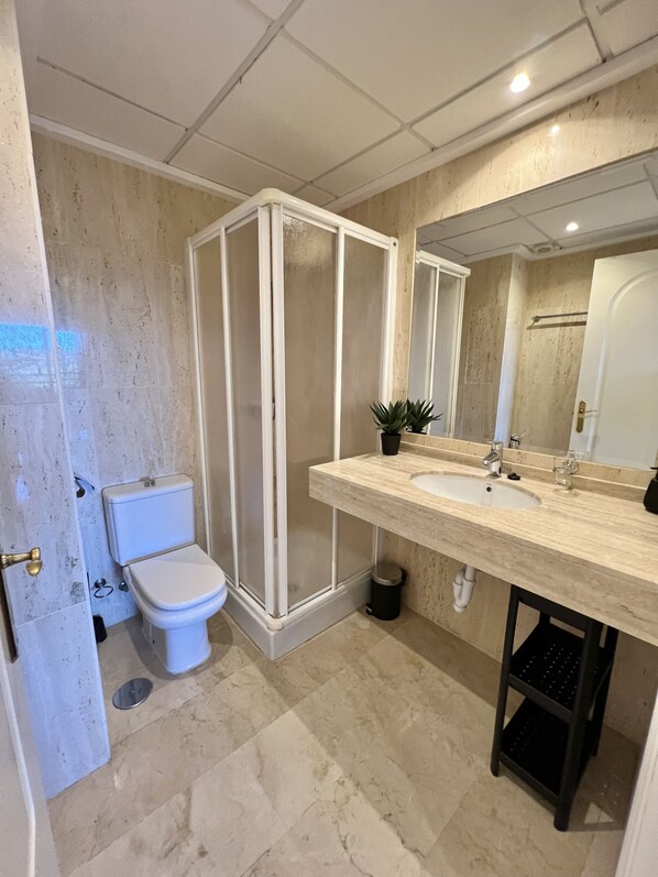 A bathroom with a toilet, a shower enclosure, a sink, and a mirror.