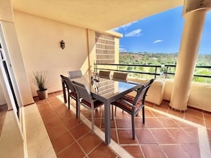 A balcony with a table and chairs, a potted plant, and a view of a residential area.