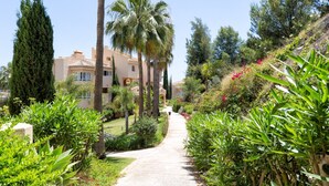 Un camí que condueix a un edifici d'estil arquitectònic mediterrani, envoltat de vegetació abundant i palmeres.