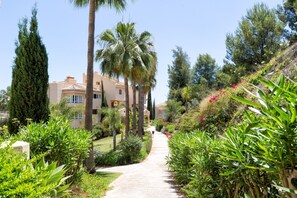 Ein Weg führt zu einem Gebäude im mediterranen Stil, umgeben von üppiger Vegetation und Palmen.