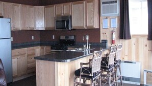 Una cocina con armarios de madera, microondas, estufa, fregadero y taburetes de bar.