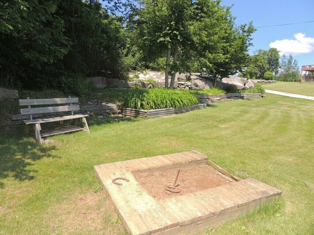 A wooden square structure with a metal ring in the center, surrounded by grass and trees.