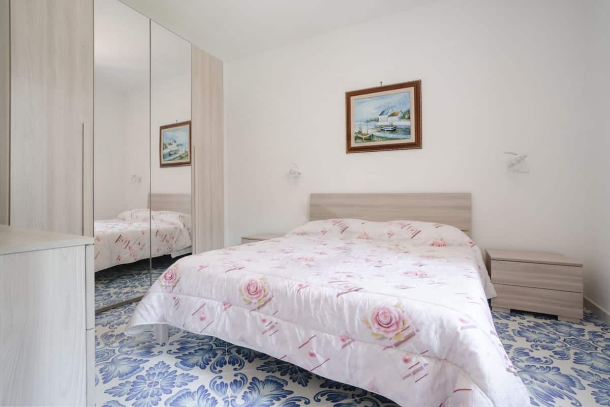 A bedroom with a bed, a dresser, a nightstand, a mirror, and a painting on the wall.