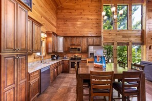 A wooden cabin interior with a kitchen, dining area, and large windows. - Beaver's Treehouse - Private Pool, Theater, Mountain Views, and Close to Pigeon Forge Parkway! (Pigeon Forge)