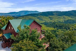 Une cabane en rondins surmontée d’un toit végétalisé, entourée d’une végétation luxuriante et avec des montagnes en arrière-plan.