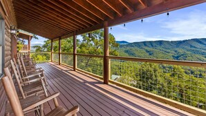 A wooden deck with chairs, a covered area, and a view of a mountainous landscape. - Beaver's Treehouse - Private Pool and Sauna! (Pigeon Forge)