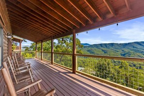 Une terrasse en bois avec des chaises, un espace abrité et une vue sur un paysage montagneux.