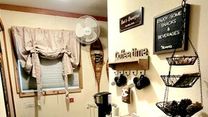 A compact kitchen with a refrigerator, a coffee machine, and a fan. There are signs on the wall indicating a breakfast area and a coffee station. - Snowy River @ big Powderhorn (Bessemer)