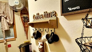 A cozy kitchen area with a coffee station, mugs hanging on hooks, and a sign that reads "Enjoy some snacks & beverages." - Snowy River @ big Powderhorn (Bessemer)