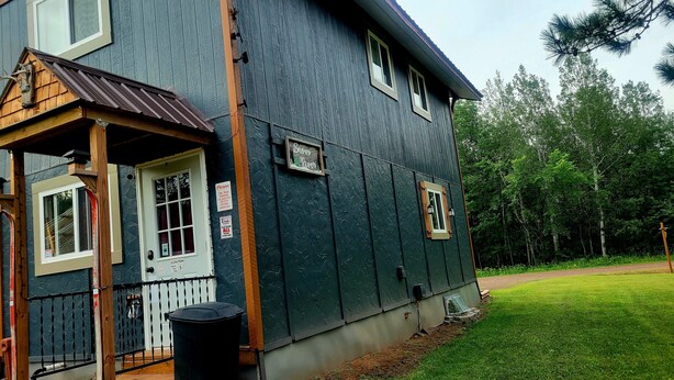 A large house with a dark exterior, a wooden porch, and a small window with a sign. - Snowy River @ big Powderhorn (Bessemer)