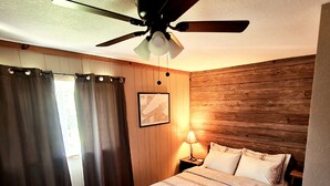 A bedroom with a bed, a ceiling fan, a nightstand, a lamp, and a window with curtains. - Snowy River @ big Powderhorn (Bessemer)