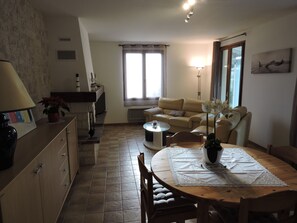 A cozy living room with a sofa, a dining table with chairs, a fireplace, and a window with curtains. - Quiet house in a private dead end 150m from the beach. (Saint-Denis-d'Oléron)
