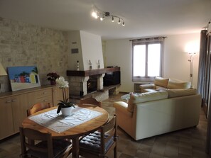 A living room with a fireplace, a sofa, a dining table with chairs, and a painting on the wall. - Quiet house in a private dead end 150m from the beach. (Saint-Denis-d'Oléron)
