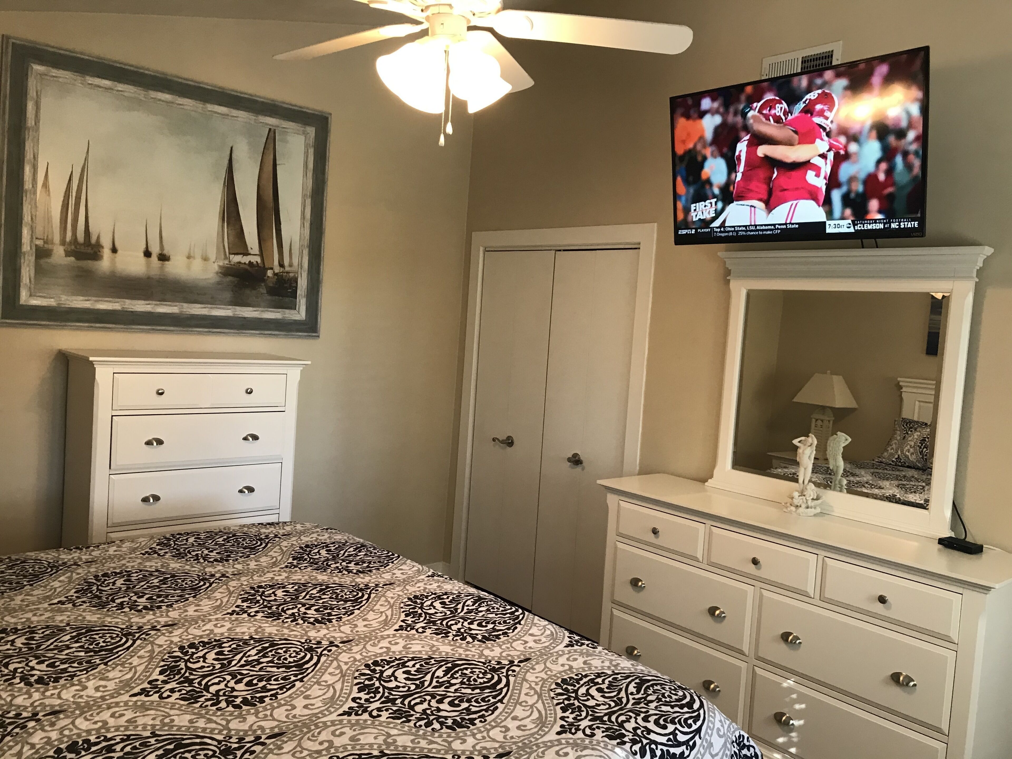 A bedroom with a bed, dresser, and a television displaying a sports event.