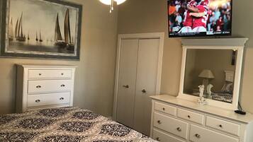 A bedroom with a bed, dresser, and a television displaying a sports event.