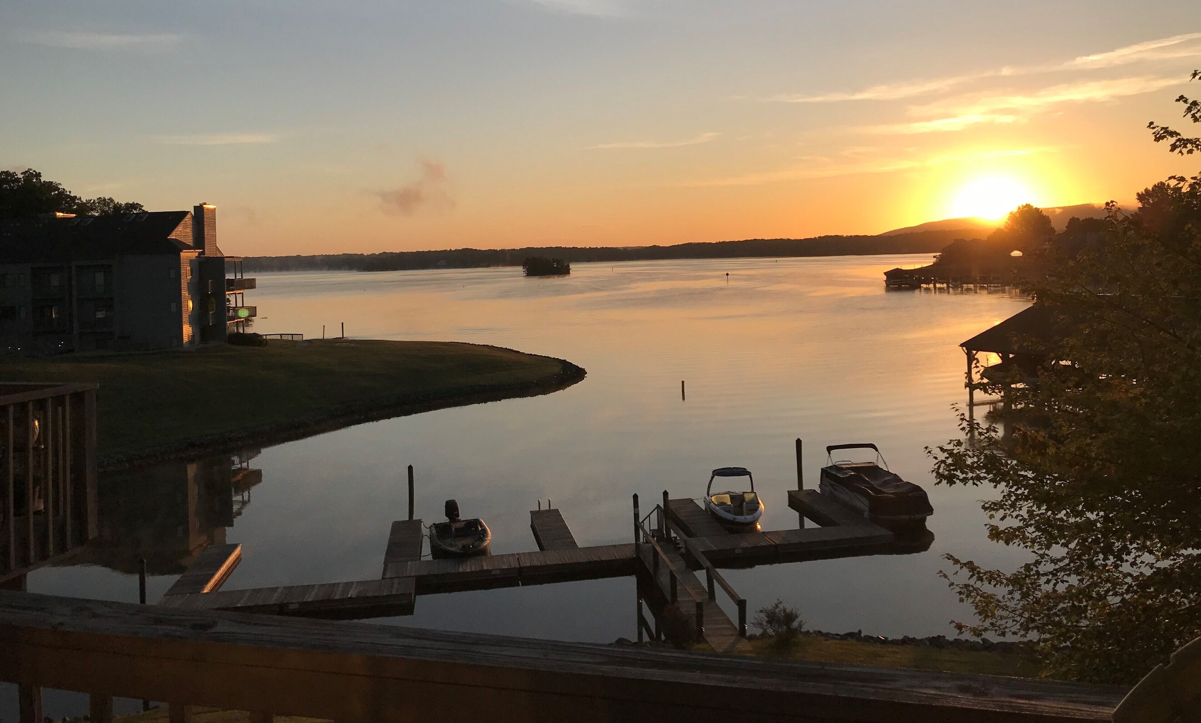 A sunset view over a calm lake with a dock and boats.