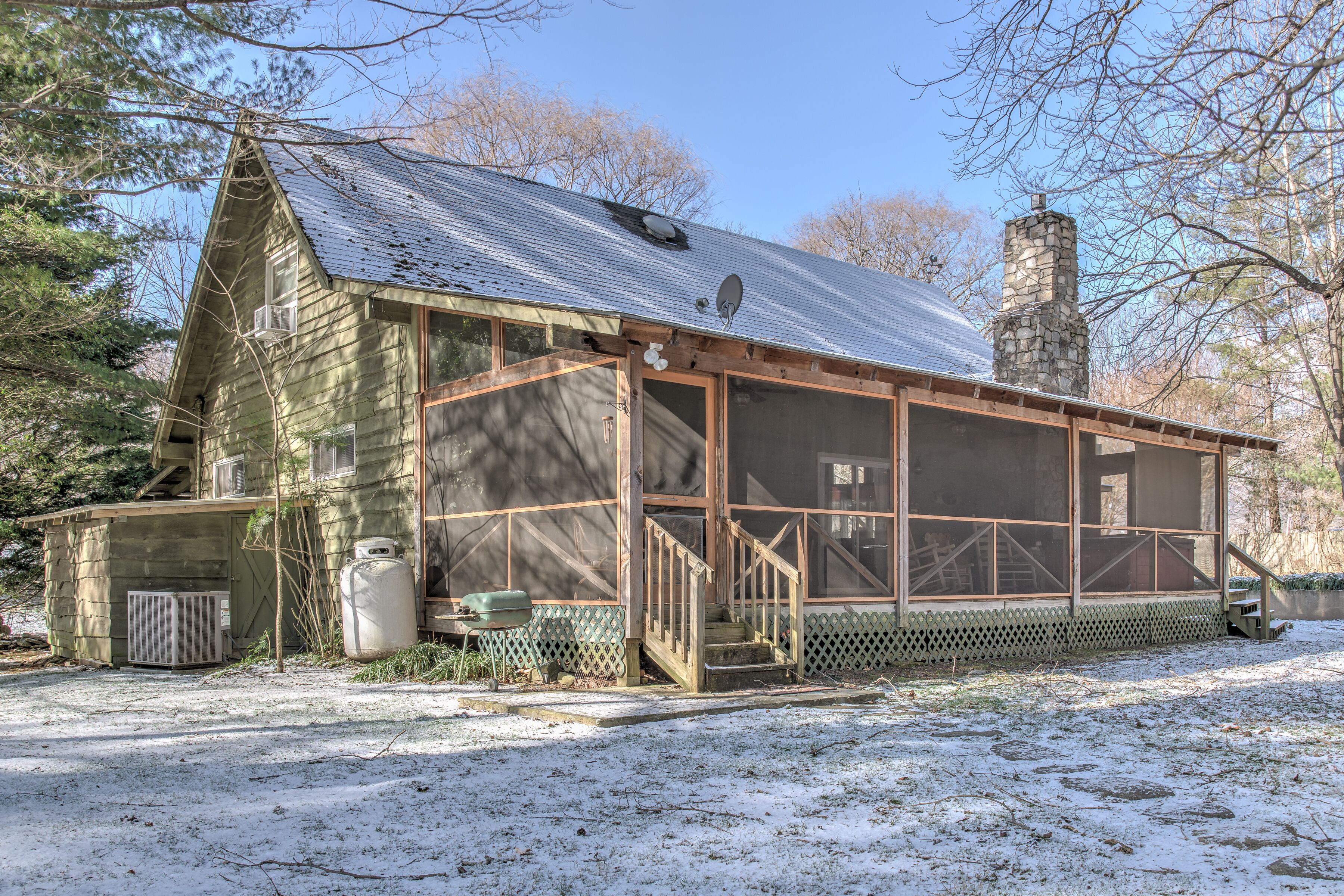 A rustic cabin with a screened porch, a stone chimney, and a wooden deck.