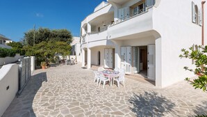 A white building with a stone courtyard, a balcony, and a table set for dining.