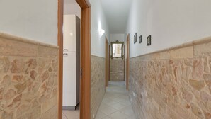 Un pasillo con paredes de piedra y suelo de baldosas, que conduce a una habitación con una puerta.