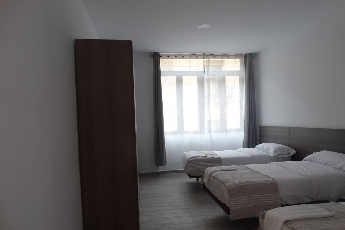 Camera d'albergo con due letti, un armadio in legno e una finestra con tende.