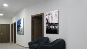Ein Korridor mit zwei Sesseln, einer Tür mit der Aufschrift '2' und zwei großen abstrakten Gemälden an den Wänden.