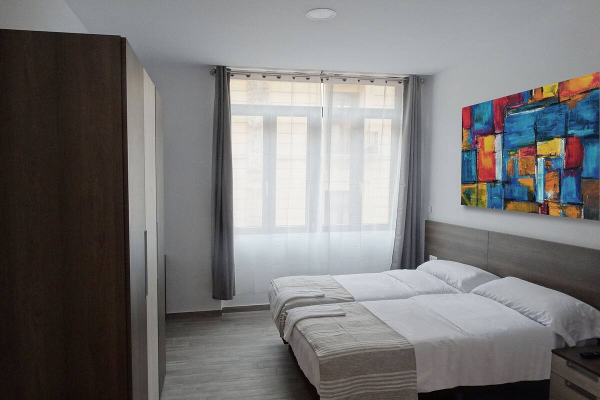 Camera da letto moderna con un letto grande, un armadio, un comodino e un quadro astratto dai colori vivaci appeso al muro.