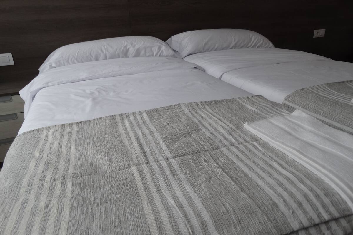 Un letto rifatto con lenzuola bianche e una coperta grigia a fantasia.