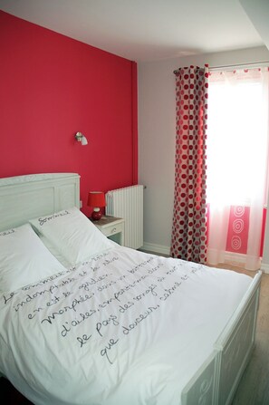 A bedroom with a white bed, red walls, a white nightstand, a red lamp, and a window with a polka dot curtain. - Chambres d'Hotes Restaurant l'Horizon des Landes (Doazit)