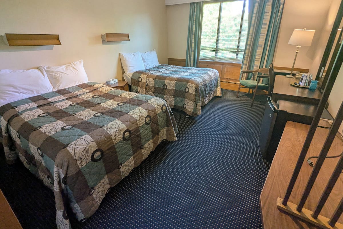 Ein Hotelzimmer mit zwei Betten, einem Schreibtisch, einem Stuhl, einer Lampe und einem Fenster mit Vorhängen.
