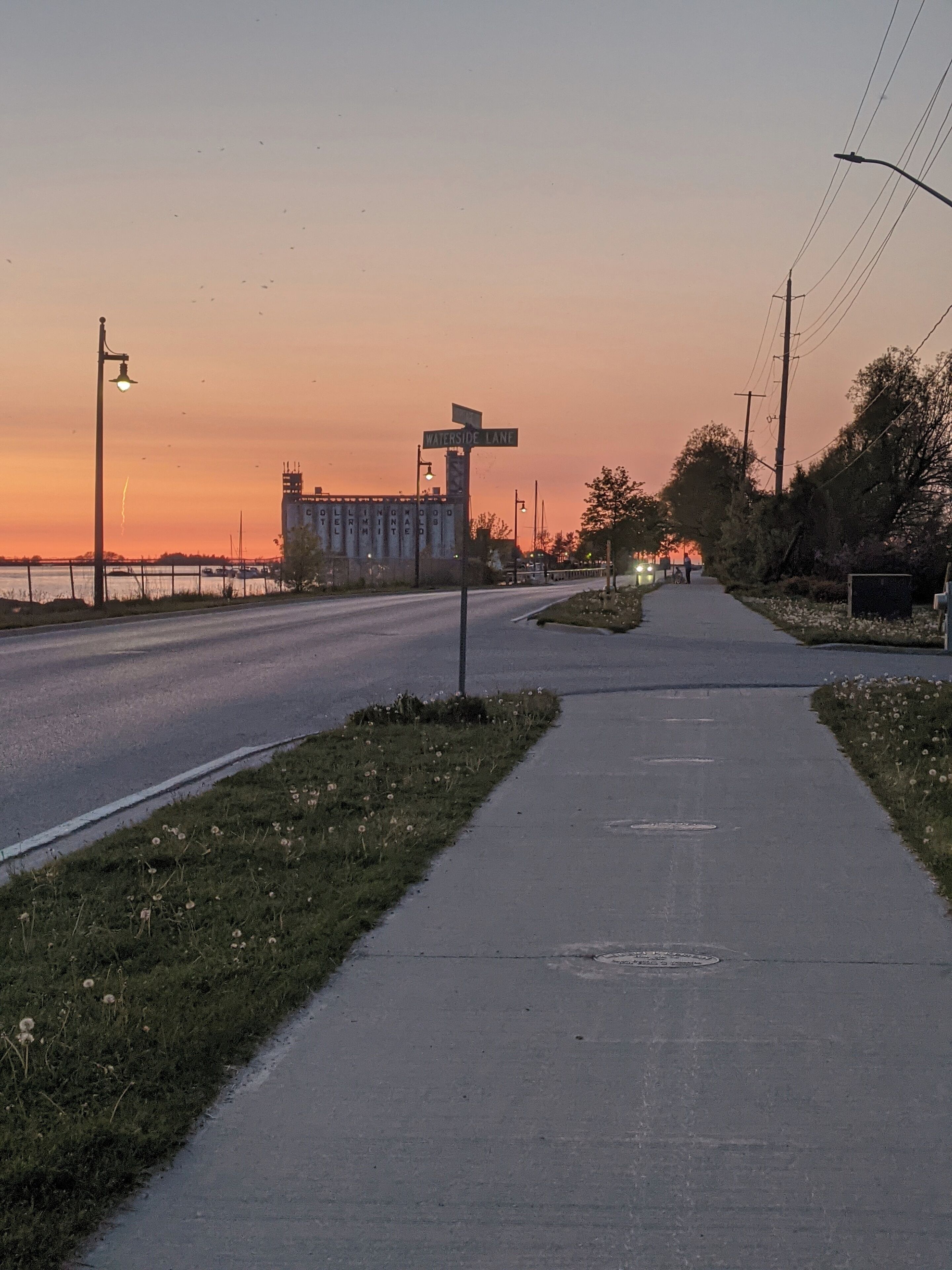 Een weg die naar een gebouw leidt, met een bord waarop 'WATERSIDE LANE' staat, bij zonsondergang.